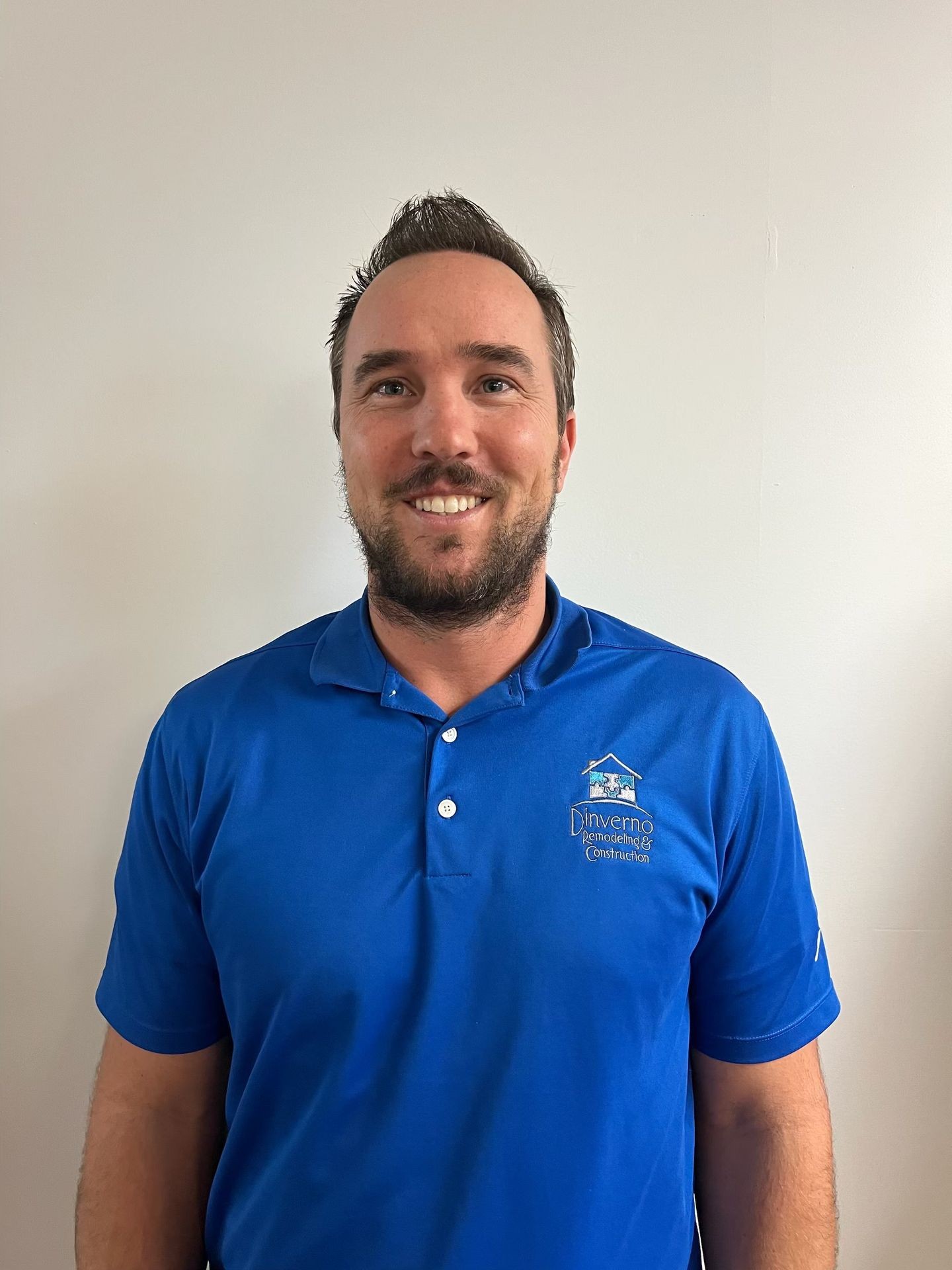 Person wearing a blue polo shirt with a logo, standing against a plain wall.