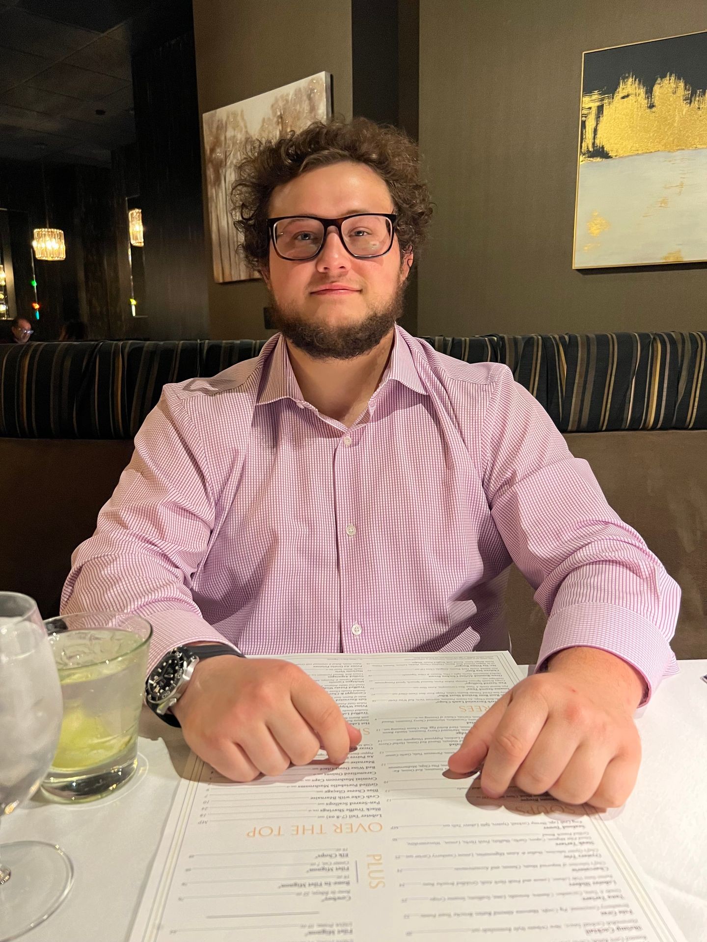 Person wearing glasses sitting at a restaurant table with a menu in front of them and drinks beside.