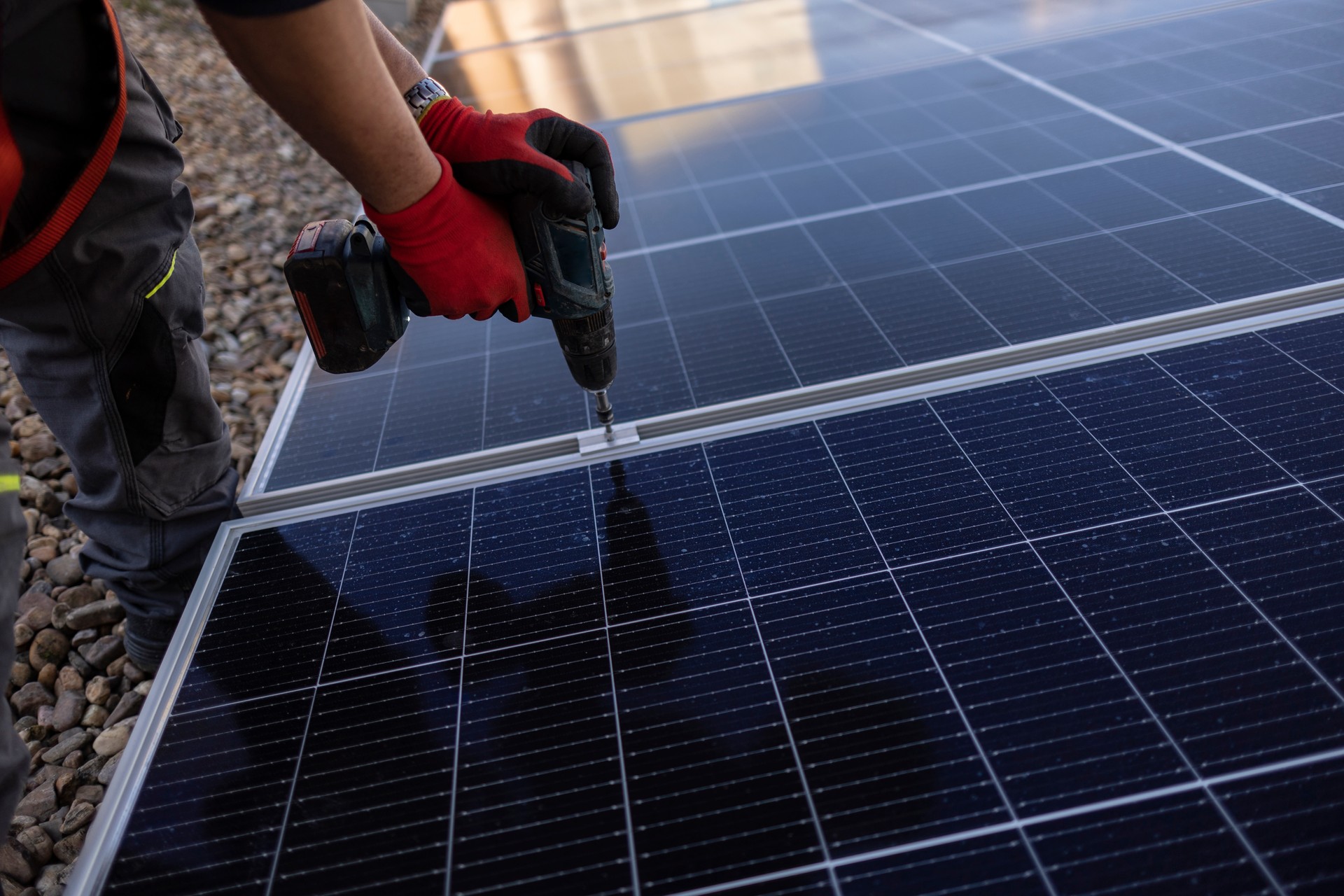 Solar panel technician with drill installing solar panels on roof. technician installing photovoltaic blue solar modules with screw. Electrician panel sun sustainable resources